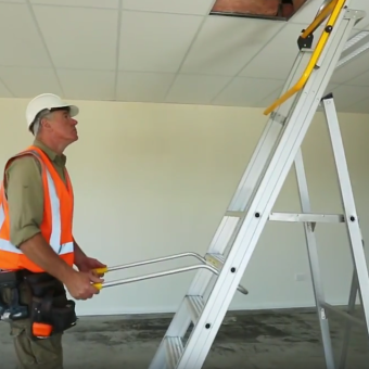 Technician towing folded Omni Platform Ladder across gravel surface